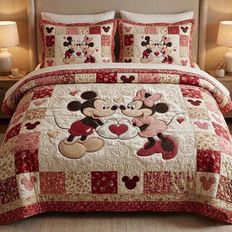 May include: A quilted bedspread and two pillow shams featuring Mickey and Minnie Mouse. The bedding has a patchwork design with red, pink, and cream squares. Mickey and Minnie are embroidered on the quilt, holding a heart. The pillow shams have the same design.