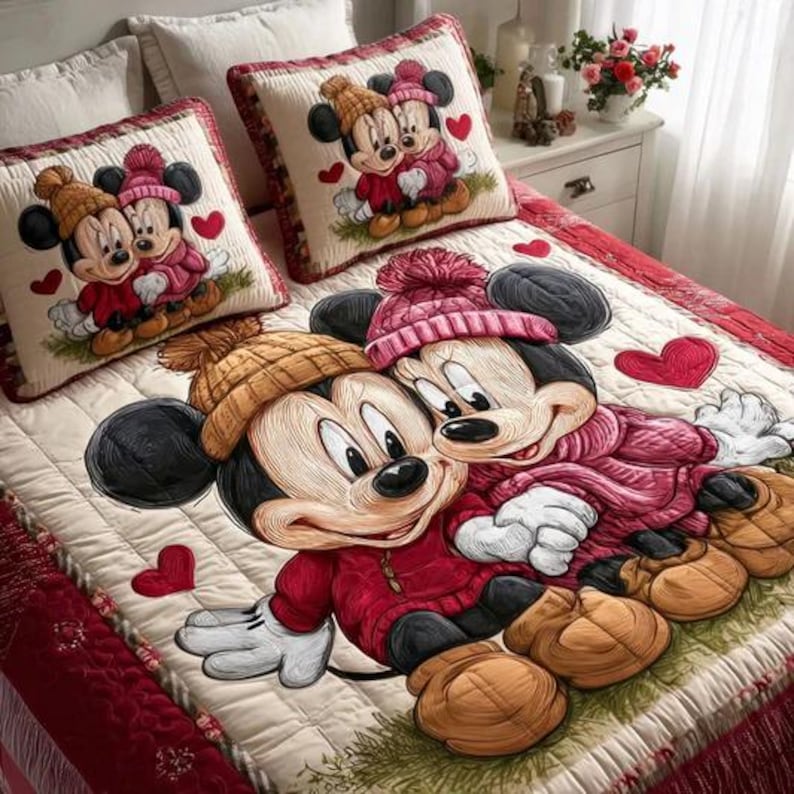 May include: A bedding set featuring Mickey and Minnie Mouse in winter attire. The set includes a quilt and two matching throw pillows. The quilt and pillows have a cream background with red accents and heart details. Mickey and Minnie are wearing hats and coats.