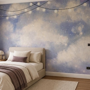 Op de afbeelding: Een muurschildering met een dromerige lucht in aquarel-stijl met zachte blauwe en witte wolken, geaccentueerd door een lichtsnoer dat bovenaan is gedrapeerd. De muurschildering creëert een serene sfeer in een slaapkamer met een neutraal bed.