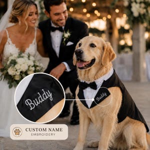 May include: A black and white dog tuxedo featuring a white shirt collar, a black bowtie, and a black vest. The vest is embroidered with the name Buddy in white cursive script. The garment is designed for a dog to wear at formal events.