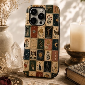 May include: A smartphone case featuring a grid of various tarot card illustrations, including symbols like a sun, a cat, a skeleton, and floral motifs in muted tones of red, green, blue, and gold, with a triple camera cutout at the top left.