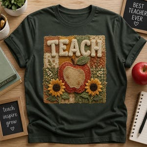 Pode incluir: Uma t-shirt verde-escura com um gráfico central em forma de quadrado estilo patchwork. O design inclui a palavra TEACH em letras texturizadas sobre uma ilustração de uma maçã vermelha ladeada por dois girassóis amarelos sobre padrões.