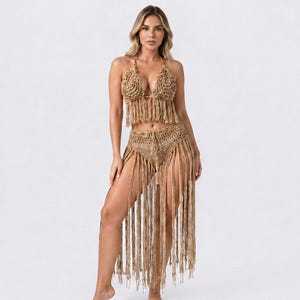 Peut inclure: Un ensemble deux pièces en crochet de couleur beige clair, composé d'un haut court style dos nu avec un motif triangulaire et d'une jupe taille haute assortie. Les deux pièces présentent de longues franges pendantes descendant jusqu'aux jambes.