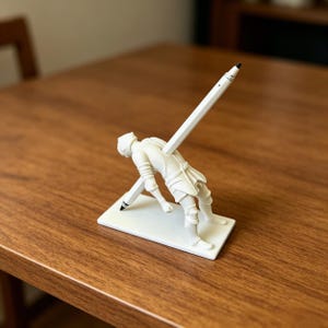 May include: A white matte finish pen holder shaped like a knight in armor leaning backward. The knight is mounted on a rectangular base and features a long white pen inserted through the back, extending through the torso to touch the base.