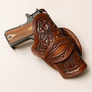 May include: A dark brown leather holster featuring intricate floral tooling and a smooth central strap, containing a semi-automatic pistol with a dark metal frame and textured wooden grip panels, captured from an angled top-down perspective.