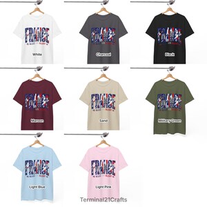 Puede incluir: Una colecci&oacute;n de camisetas de manga corta en blanco, carb&oacute;n, negro, granate, arena, verde militar, azul claro y rosa claro. Cada camiseta presenta un estampado gr&aacute;fico con el texto FRANCE y ALLEZ LES BLEUS en azul, blanco y rojo.