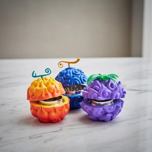 May include: Three round herb grinders with textured, fruit-like shells in orange-yellow, blue, and purple. Each grinder features a metallic interior mechanism and a small, stylized stem on top, mimicking the appearance of fantasy-inspired fruits.