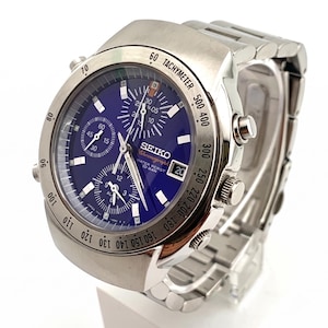 May include: A silver-tone stainless steel Seiko chronograph watch with a deep blue dial, three sub-dials, a date window at the three o'clock position, and a tachymeter bezel. The watch features a metal link bracelet and luminous hour markers.