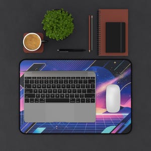 Può includere: Vista dall'alto di una postazione di lavoro con laptop, mouse e tappetino per mouse dal design retrò nei toni del blu, viola e rosa. Una tazza di caffè, una piccola pianta e articoli di cancelleria completano l'ambiente.