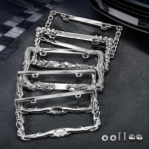 May include: A collection of four rectangular chrome license plate frames with distinct metallic designs, including skull motifs, dragon figures, and chain-link patterns. The set includes small metal hardware components like screws and caps.