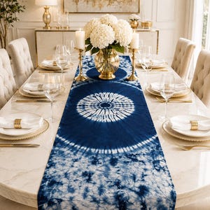 May include: A long rectangular table runner featuring a deep blue and white tie-dye pattern with circular mandala-like motifs. The fabric displays a gradient of intricate, crinkled textures and radial designs centered along the length of the runner.