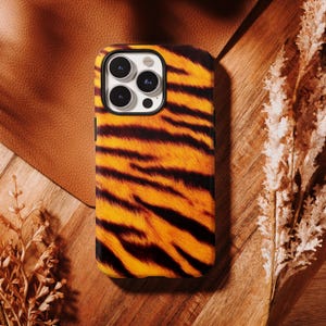 May include: A smartphone case featuring a vibrant orange and black tiger stripe pattern. The case has a rectangular shape with rounded corners and a cutout at the top left corner for a triple-lens camera system, showing the black camera housing.