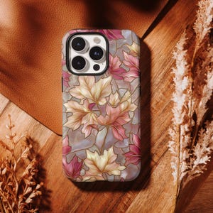 May include: A smartphone case featuring a stained glass pattern of maple leaves in shades of pink, cream, and soft brown. The design includes dark outlines separating the leaf shapes, with a triple camera cutout located at the top left corner.