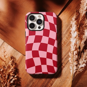 May include: A smartphone case featuring a wavy, distorted checkerboard pattern in alternating shades of deep red and light pink. The case has a black camera cutout area with three circular lenses and a flash, covering the back of the device.