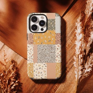 Könnte beinhalten: Eine Smartphone-Hülle mit einem Patchwork-Design aus verschiedenen Blumen- und Punktemustern in Senfgelb, Salbeigrün, Creme und gedämpftem Orange. Die Hülle hat einen schwarzen Kameraausschnitt und bedeckt die Rückseite des Geräts.