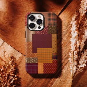 Pode incluir: Uma capa de smartphone com um design de patchwork de vários padrões em tons de outono, incluindo xadrez, bolinhas e pequenas estampas florais em tons de bordô, amarelo mostarda, castanho e creme, com um recorte para a câmara de três lentes.