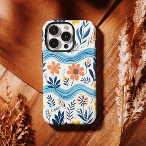 May include: A smartphone case featuring a cream-colored background with a pattern of orange flowers, dark blue leaves, and yellow accents. The design includes horizontal wavy light blue lines that span across the surface of the phone case.