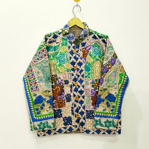 May include: A long-sleeve jacket featuring a vibrant patchwork design with various floral and paisley patterns in shades of blue, green, purple, and gold. The jacket has a collared neckline, a front button closure with light brown buttons, and long sleeves.