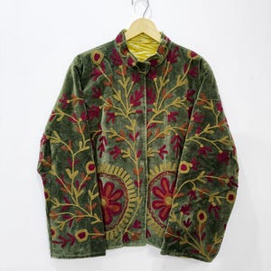 Peut inclure: Une veste en velours vert olive ornée de broderies complexes dans des tons jaune moutarde et magenta profond. Le motif présente des fleurs et des vignes sur les panneaux avant, un col montant et des manches longues, présentée sur un cintre en bois.