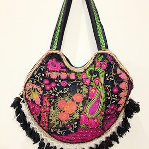 Puede incluir: Un bolso tote negro con intrincados bordados florales y de cachemira multicolor en tonos rosa, naranja y verde. El bolso tiene correas negras para el hombro con ribete verde y está decorado con borlas negras y cuentas blancas en la parte inferior.