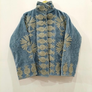 May include: A light blue velvet jacket featuring a high collar and long sleeves. The garment is decorated with intricate, raised embroidery in a muted gold tone, displaying repeating floral motifs and stylised pomegranate shapes.
