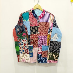 Puede incluir: Una chaqueta acolchada de manga larga con un diseño de patchwork que presenta varios patrones florales, geométricos y de cachemira en tonos rojos, azules, rosas y blancos. La chaqueta tiene cuello mao, cierre frontal de botones y dos bolsillos.