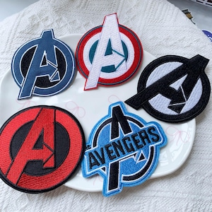 Könnte beinhalten: Fünf gestickte Stoffaufnäher mit dem Avengers-Logo. Ein Aufnäher ist dunkelblau, einer rot-weiß, einer schwarz-weiß, einer rot-schwarz und einer hellblau mit dem in das Design integrierten Schriftzug THE AVENGERS.