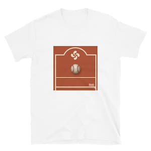 Puede incluir: Una camiseta blanca de manga corta con un gráfico cuadrado centrado. El diseño muestra una cancha de color terracota con un símbolo lauburu blanco en la parte superior, una pelota de béisbol en el centro y el texto BbasK impreso en blanco abajo.