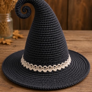 Peut inclure: Un chapeau en crochet gris anthracite foncé avec un sommet haut, pointu et recourbé. Le chapeau présente un large bord plat et une bande décorative en dentelle festonnée de couleur crème entourant la base de la calotte, en maille texturée.