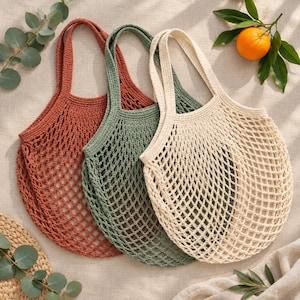 Peut inclure: Trois sacs de marché en crochet de couleur orange rouille, vert sauge et blanc crème. Chaque sac présente un motif en filet à losanges larges avec des anses solides et renforcées ainsi qu'une base arrondie, conçus pour transporter des objets.