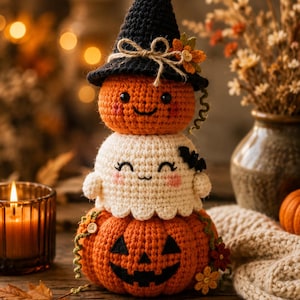 Può includere: Una figura all'uncinetto impilata composta da una grande zucca arancione alla base, un fantasma bianco al centro e una piccola zucca arancione con un cappello da strega nero in cima. Il fantasma ha un piccolo pipistrello nero e dettagli floreali.