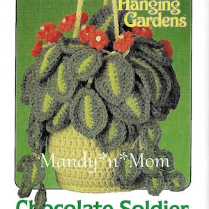 Puede incluir: Un patrón de crochet para una planta colgante con hojas verdes y flores rojas. El patrón se titula "Jardines colgantes" y es de "Mandy 'n' Mom". El patrón se llama "Chocolate Soldier" y es de Barbara Anderson.
