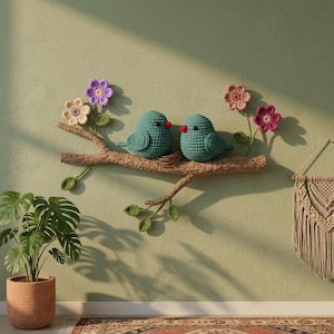 May include: A wall-mounted decorative piece featuring two teal crocheted birds perched on a brown branch. The branch is adorned with crocheted green leaves and flowers in shades of cream, purple, pink, and magenta, with a small nest between the birds.