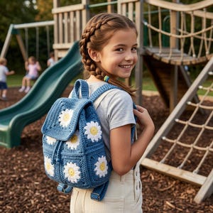 May include: A blue crochet backpack featuring a pattern of white and yellow daisy motifs. The bag has a flap closure with a drawstring, adjustable straps, and metal hardware. The design is constructed from square panels with a textured yarn finish.