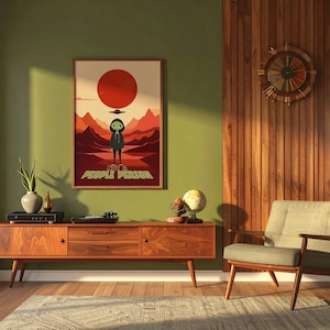 May include: A rectangular framed wall art print featuring a stylized illustration of a hooded figure standing in a desert landscape under a large red sun and a flying saucer, with the text NOT A PEOPLE PERSON printed in yellow at the bottom.
