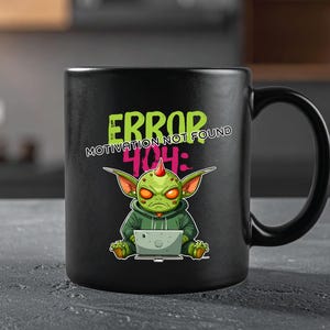 May include: Black ceramic mug featuring a cartoon alien with a laptop. The alien is green with red eyes and a hoodie. The mug has the text "ERROR 404: MOTIVATION NOT FOUND" in green and white.