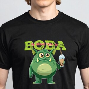 May include: Black t-shirt with a green monster illustration holding a boba tea. The words "BOBA is" are printed above the monster in green, block letters. The monster has large eyes and a toothy grin.