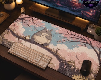 May include: A rectangular desk mat featuring a printed illustration of a grey, round creature sitting on a tree branch amidst pink cherry blossoms and a light blue sky. A white mechanical keyboard and a black computer mouse rest on the mat.