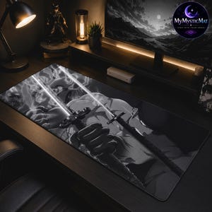 May include: A rectangular desk mat featuring a black and white graphic illustration of a character holding two swords with glowing blades. The design includes swirling smoke effects and sharp lines, covering the entire surface of the mat.