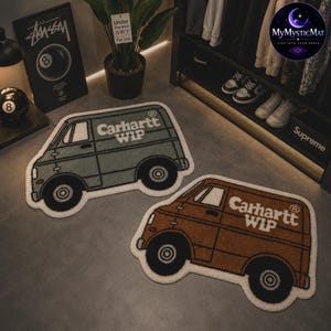 May include: Two van-shaped rugs. One is sage green, the other is brown. Both have the text "Carhartt WIP" in white. The rugs have black wheels and white outlines. The rugs are on a gray floor.
