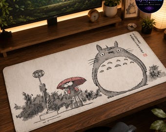 May include: A rectangular desk mat featuring a light beige background with a black ink-style illustration of a large grey creature, a person holding a red umbrella, and a bus stop sign. Japanese text is printed in the upper right corner.