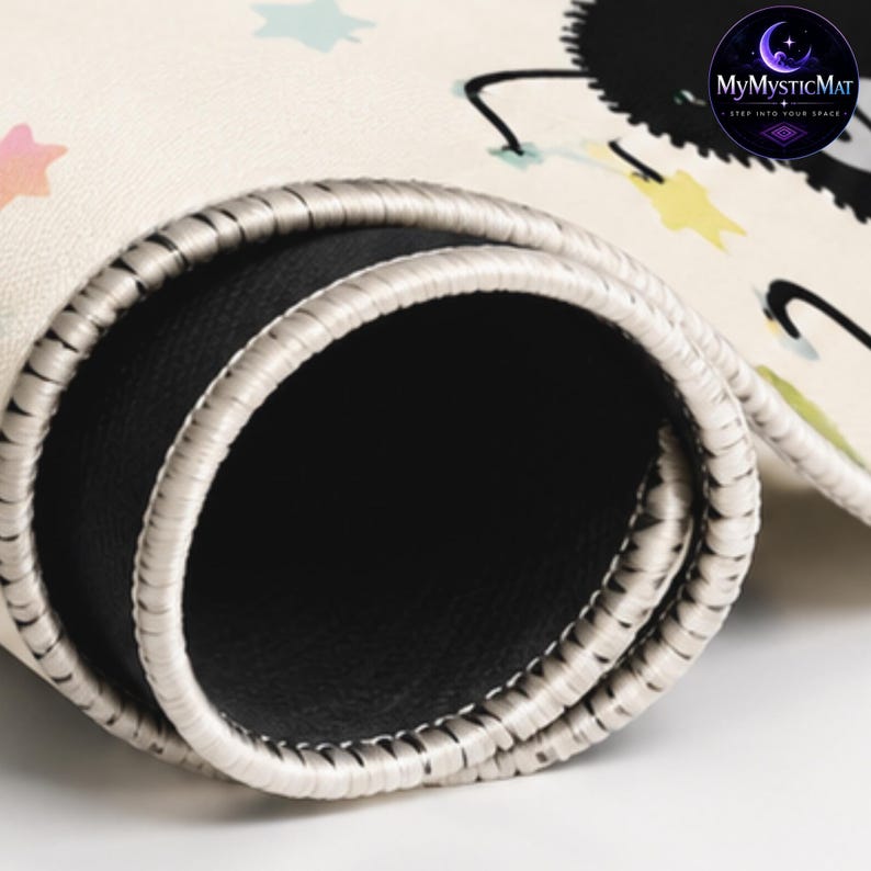 May include: A rolled-up cream-colored mat with a black circular logo reading MyMysticMat, Step Into Your Space. The mat features a pattern of small pastel-colored stars and a black character. It has a black rubberized underside and stitched edges.