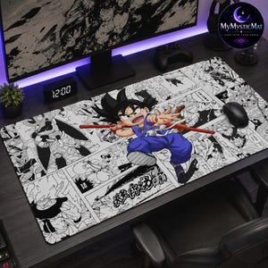 May include: A rectangular desk mat featuring a black and white manga panel collage background with a central, full-colour illustration of a young boy with spiky black hair wearing a blue outfit and holding a long red staff, positioned on a dark desk.