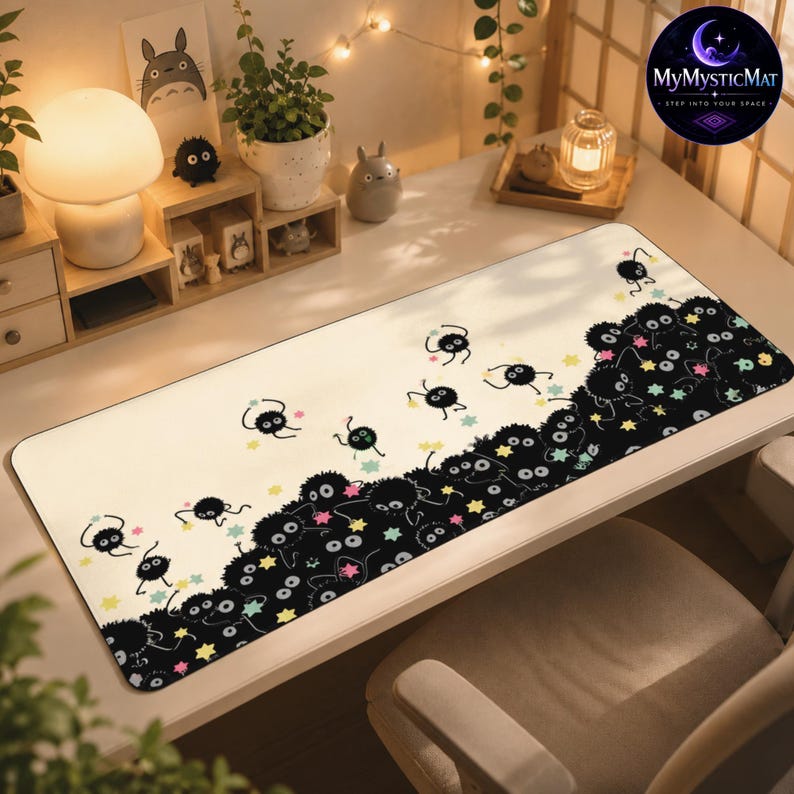 May include: A rectangular desk mat featuring a cream-colored background with a pattern of small, black, fuzzy soot sprites and colorful star shapes. The design transitions into a dense cluster of these black sprites along the bottom right edge.