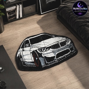 May include: A black and white car-shaped rug with red accents on the wheels. The rug is on a light wood floor. The rug has the text "MyMysticMat" in a circular logo in the upper right corner.