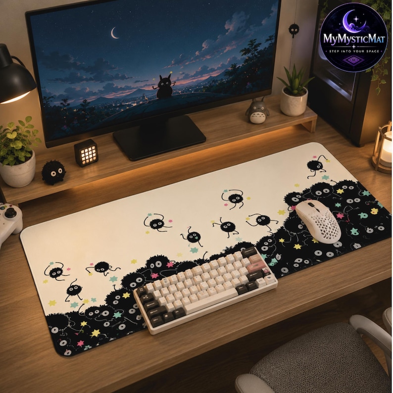 May include: A rectangular desk mat featuring a cream-colored background that transitions into a black area on the right side. The mat is decorated with numerous small, round, black soot sprites and colorful star-shaped accents scattered across the surface.