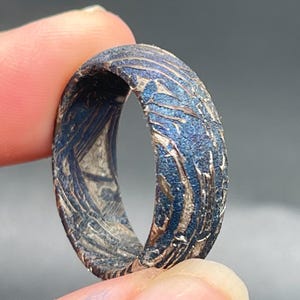 May include: A ring featuring a textured, dark blue surface with metallic silver-toned, irregular, vein-like patterns running throughout the exterior and interior. The band has a rugged, uneven finish with a deep blue hue and contrasting light metallic streaks.