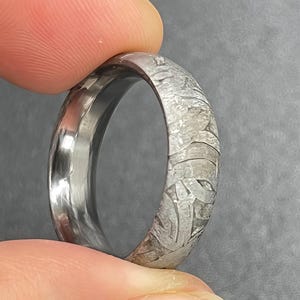 Peut inclure: Une bague en métal argenté présentant un motif de Widmanstätten distinct sur sa surface extérieure. L'anneau possède une finition intérieure lisse et polie ainsi qu'un design extérieur texturé et cristallin aux formes géométriques complexes.