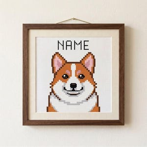 Könnte beinhalten: Ein quadratisch gerahmtes Kreuzstichbild mit einem verpixelten Corgi-Hund mit braun-weißem Fell, rosa Innenohren und einer schwarzen Nase. Das Wort NAME ist in schwarzen Blockbuchstaben über dem Kopf des Hundes auf weißem Gitterstoff gestickt.