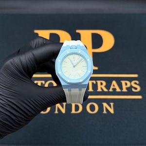 Puede incluir: Un reloj de pulsera azul claro con un bisel octogonal de ocho tornillos visibles, una esfera texturizada de color crema con manecillas plateadas y una correa de caucho azul claro a juego. La caja del reloj tiene un acabado mate.